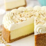 An almond mousse cheesecake on a serving platter with one slice removed and featured in the background