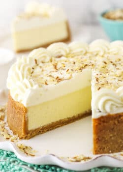 An almond mousse cheesecake on a serving platter with one slice removed and featured in the background