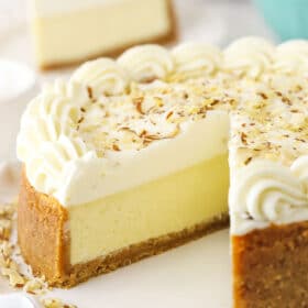 An almond mousse cheesecake on a serving platter with one slice removed and featured in the background