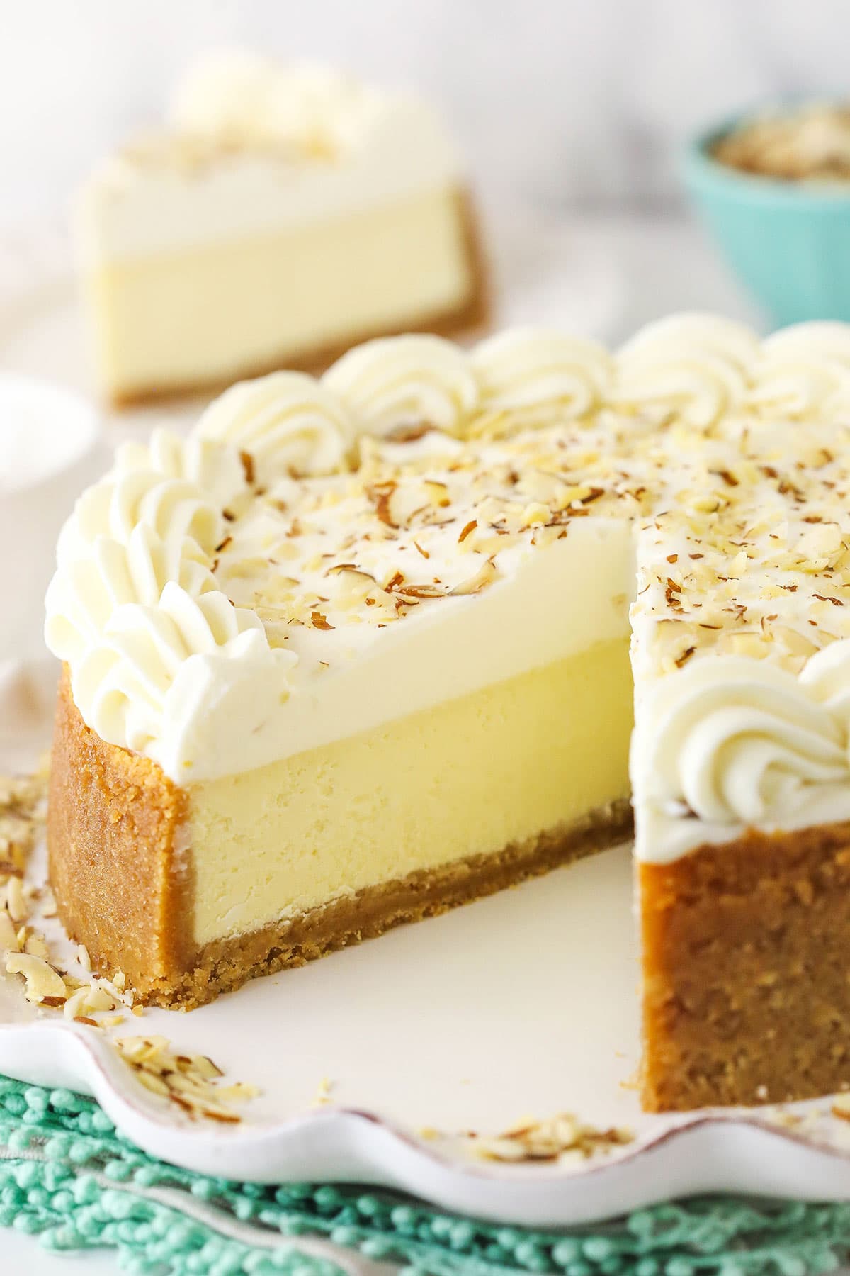 An almond mousse cheesecake on a serving platter with one slice removed and featured in the background