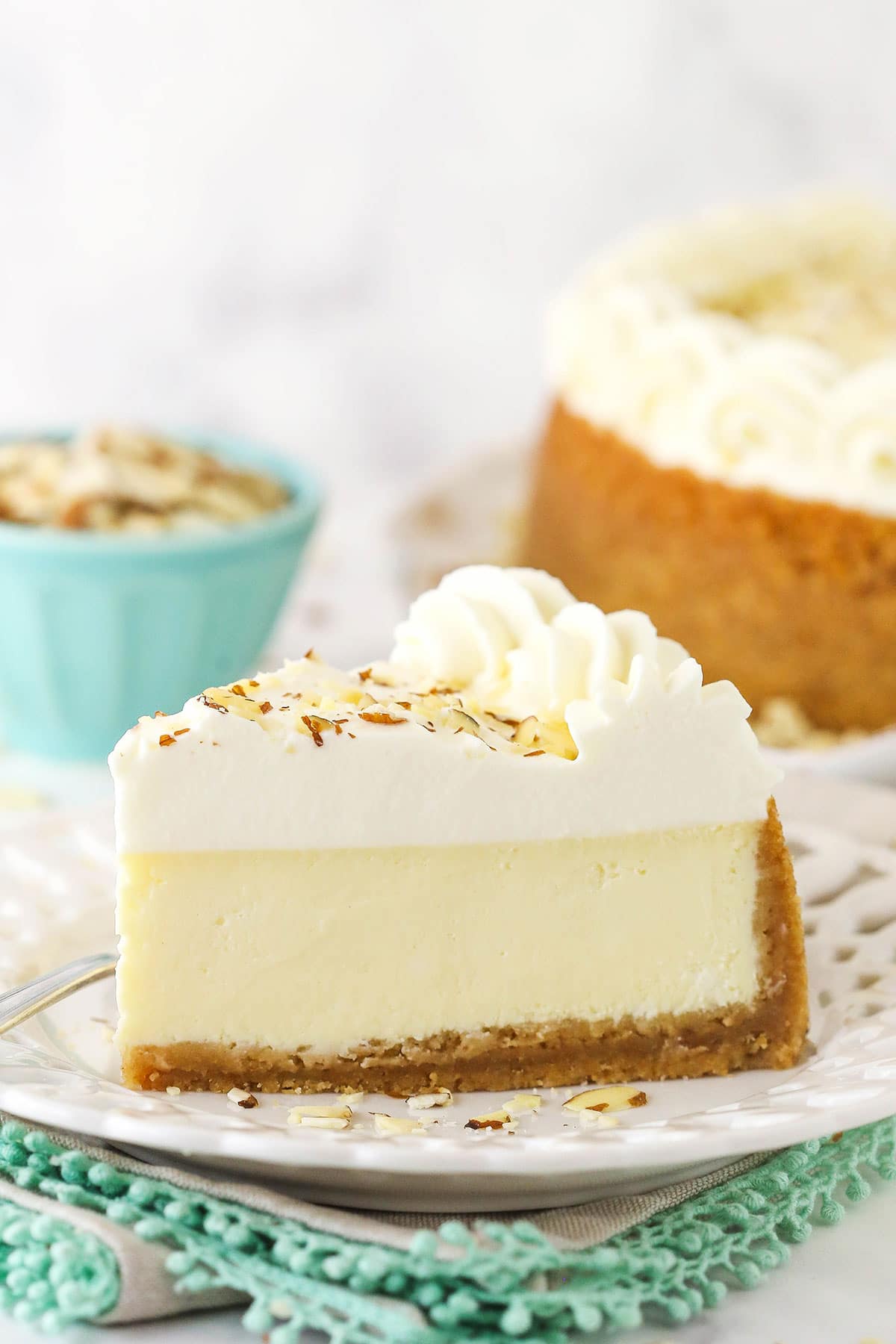 A slice of Amaretto cheesecake on a plate with a bowl of slivered almonds behind it