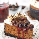 slice of black forest cheesecake on white plate with cherry topping in jar