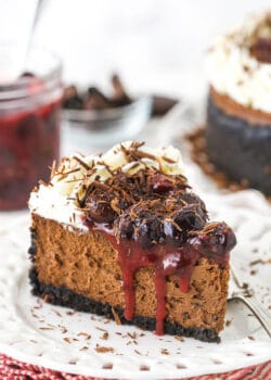slice of black forest cheesecake on white plate with cherry topping in jar