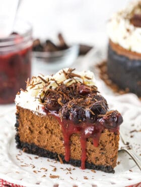 slice of black forest cheesecake on white plate with cherry topping in jar