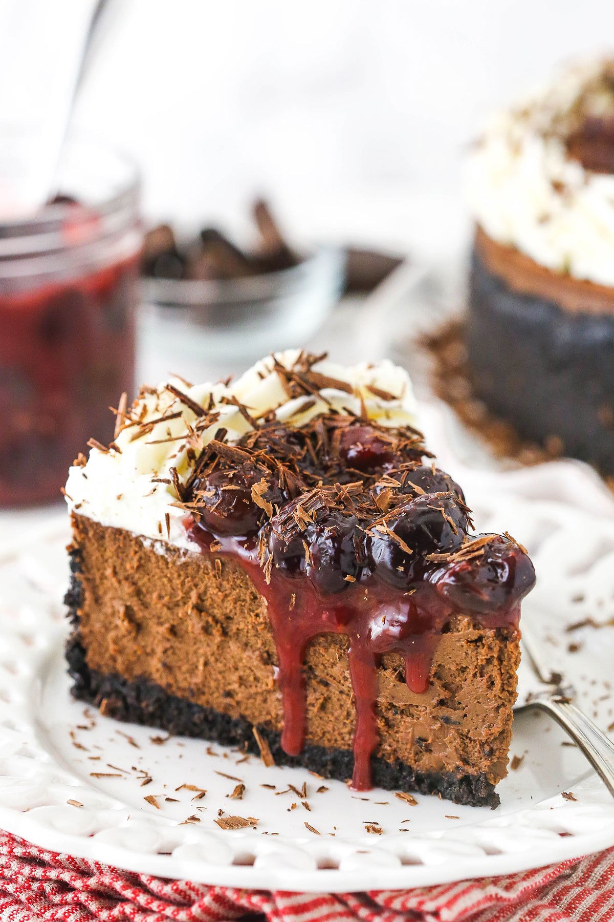 slice of black forest cheesecake on white plate with cherry topping in jar