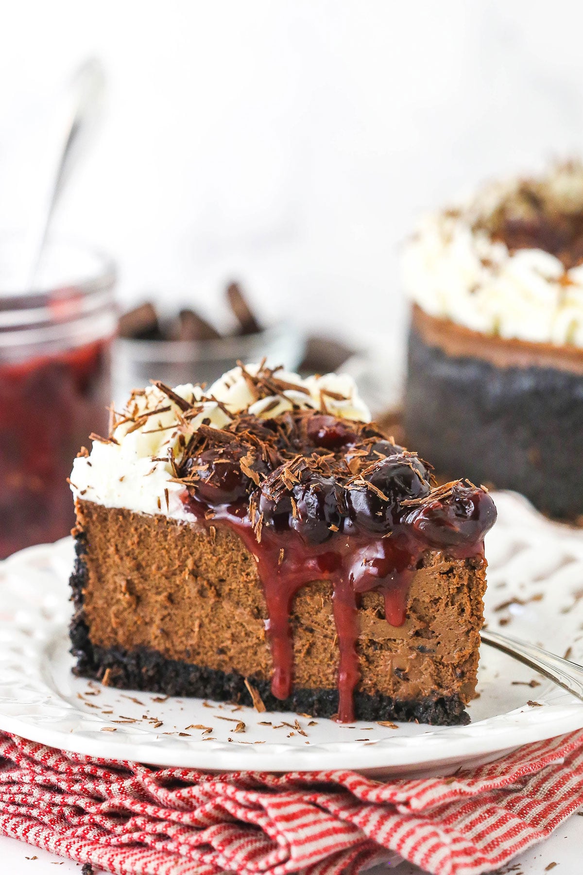 slice of chocolate cheesecake on white plate with cheesecake in background