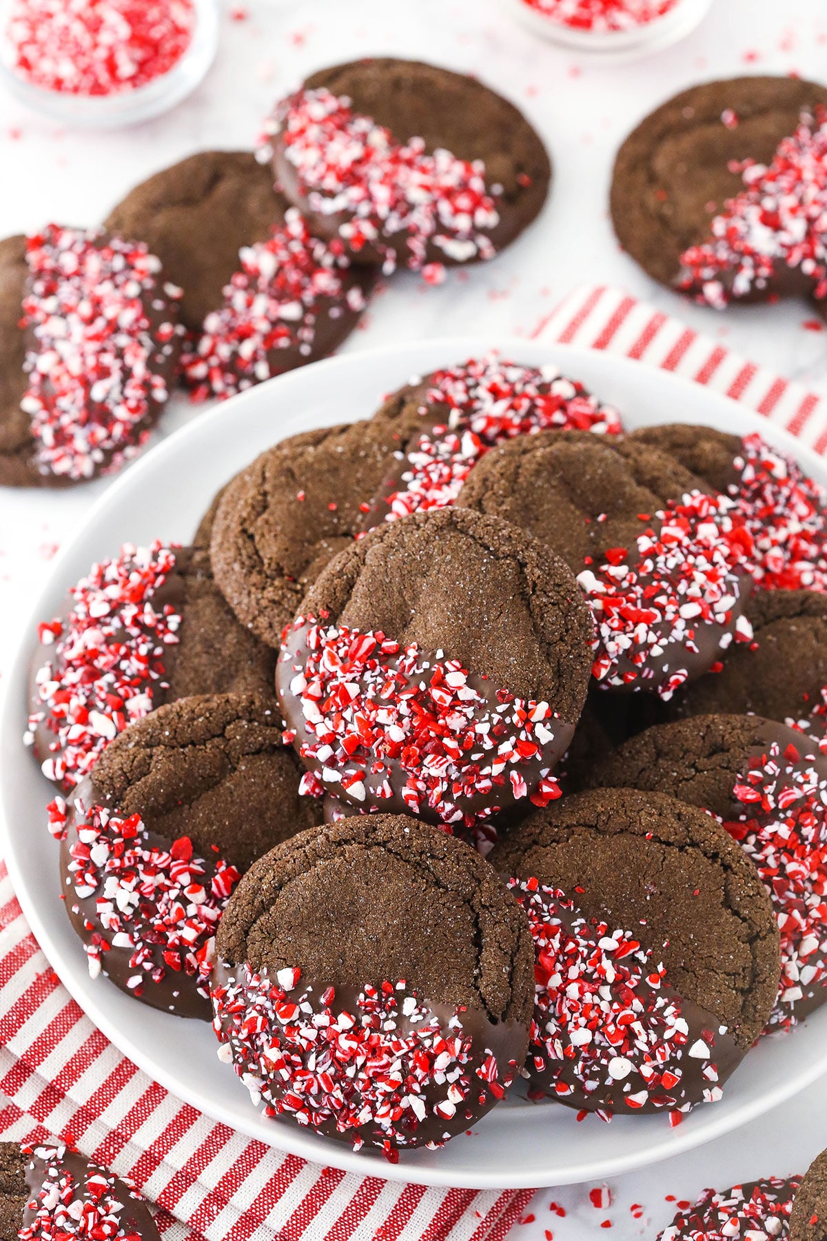 A plate piled high with chocolate peppermint sugar cookies on top of a red and white kitchen towel