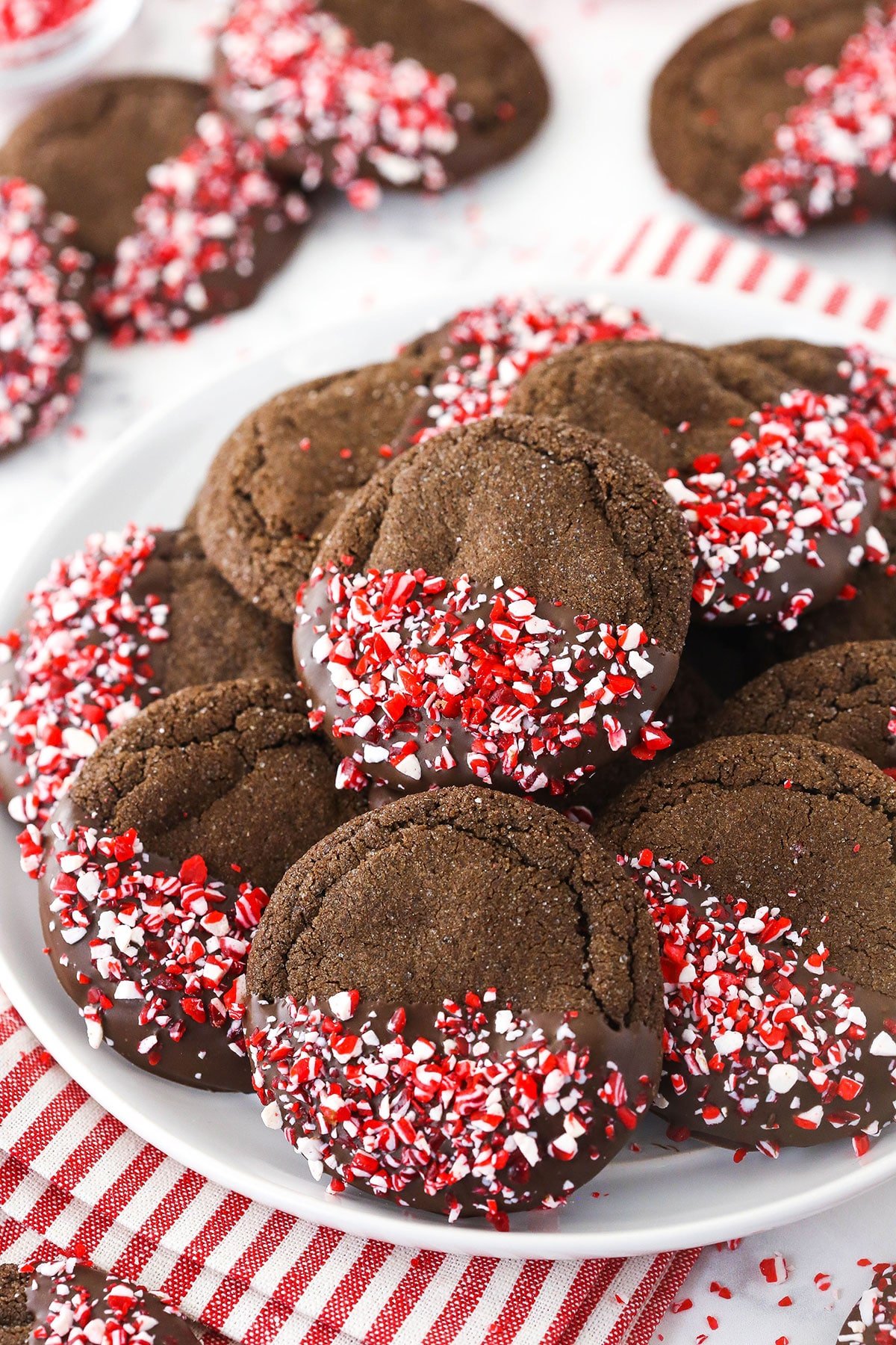 Christmas sugar cookies piled onto a large serving plate with more cookies in the background