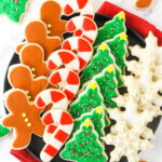 A plate full of neatly organized cut-out sugar cookies with a cloth napkin underneath it