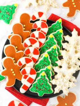 A plate full of neatly organized cut-out sugar cookies with a cloth napkin underneath it