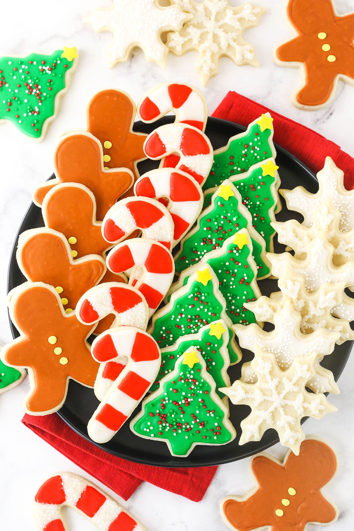 This soft sugar cookie recipe makes the most tender cookies! Paired with a classic sugar cookie icing, they're perfect for decorating. A plate full of neatly organized cut-out sugar cookies with a cloth napkin underneath it.