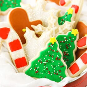 Sugar cookies shaped like snowflakes, candy canes and Christmas trees inside of a metal tin on a kitchen countertop