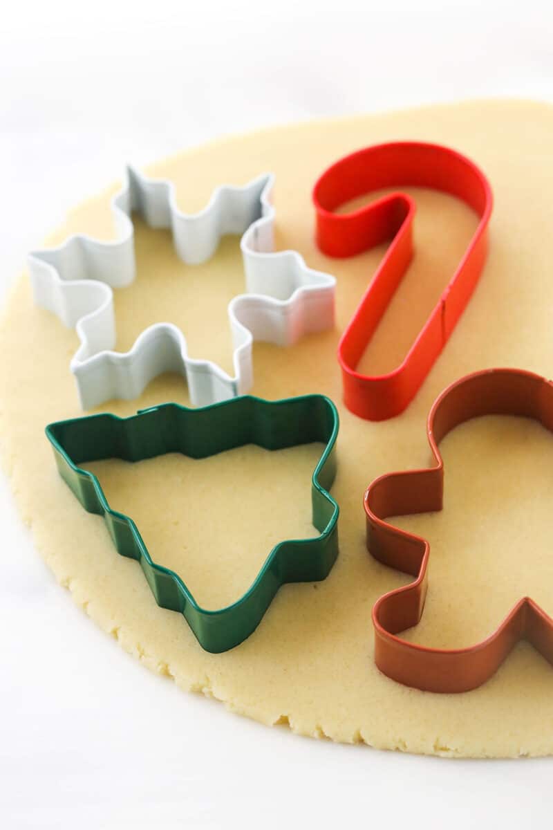 A candy cane, snowflake, Christmas tree and gingerbread man cookie cutter on top of a slab of dough.