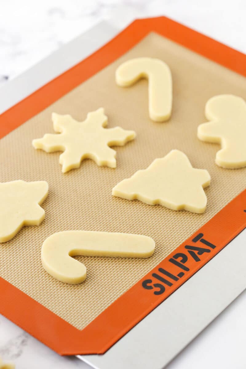 Six unbaked sugar cookies on a baking sheet covered with a Silpat liner.