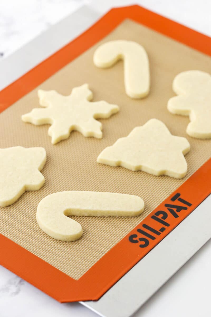 Six baked cut-out sugar cookies on a cookie sheet on top of a marble counter.