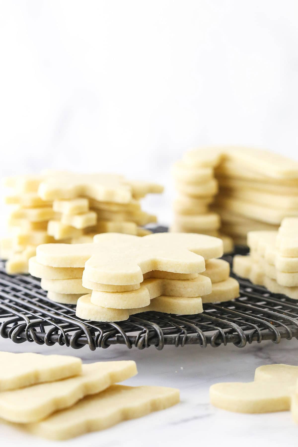 A wire rack on a countertop with sugar cookies stacked on top of it.