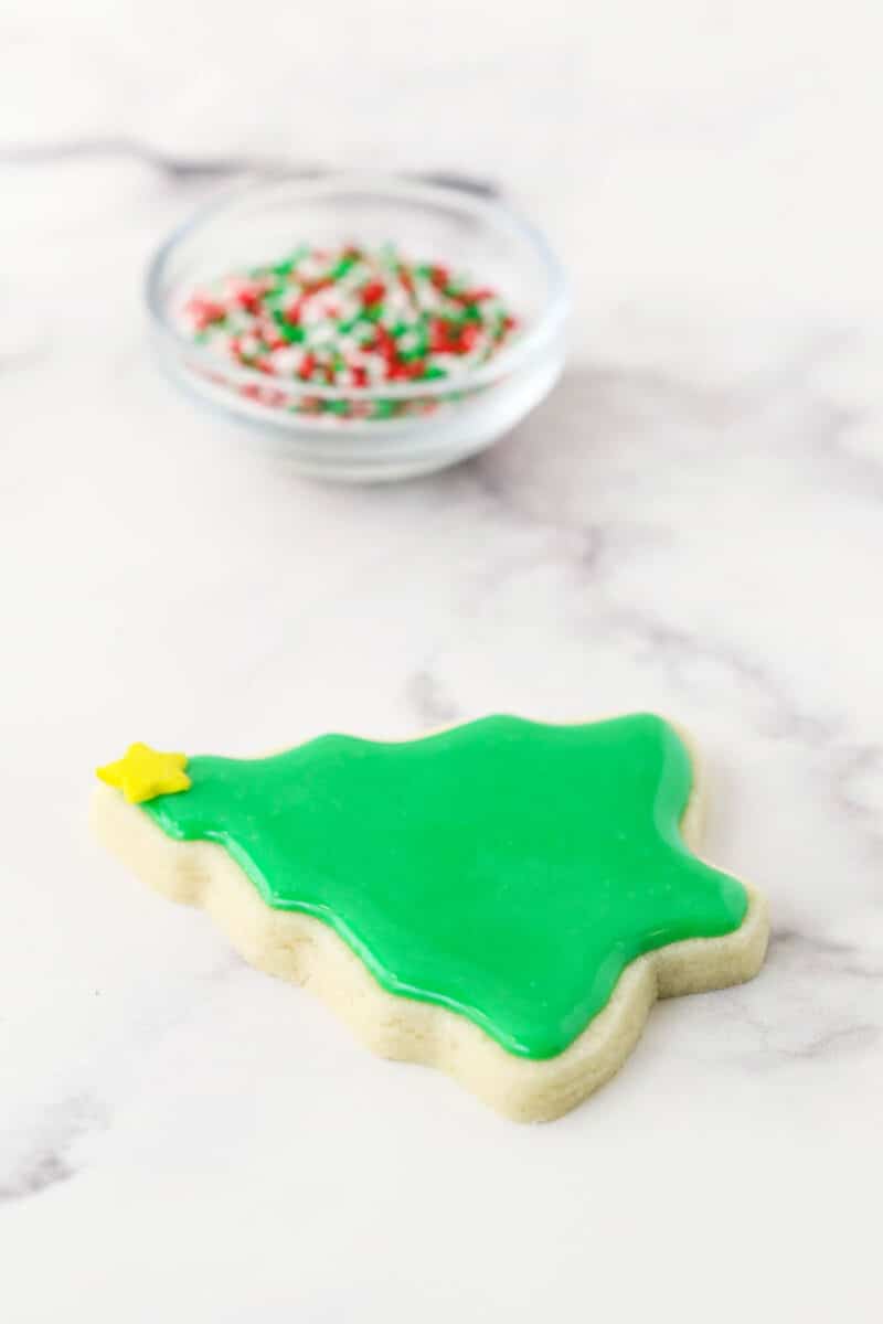 This glossy sugar cookie icing is easy to make in just 15 minutes! It hardens beautifully on top of cookies and tastes as good as it looks. A single sugar cookie in the shape of a Christmas tree with green icing on top of it