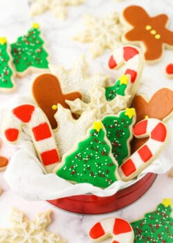 A tin full of holiday-themed sugar cookies decorated with icing on top of a granite countertop