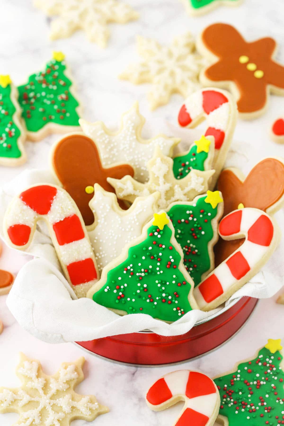 A tin full of holiday-themed sugar cookies decorated with icing on top of a granite countertop