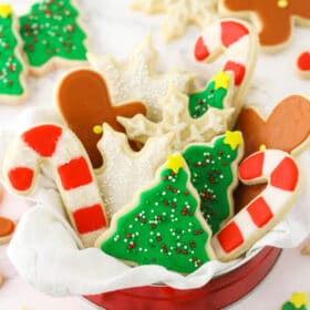 A tin full of holiday-themed sugar cookies decorated with icing on top of a granite countertop