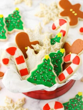 A tin full of holiday-themed sugar cookies decorated with icing on top of a granite countertop