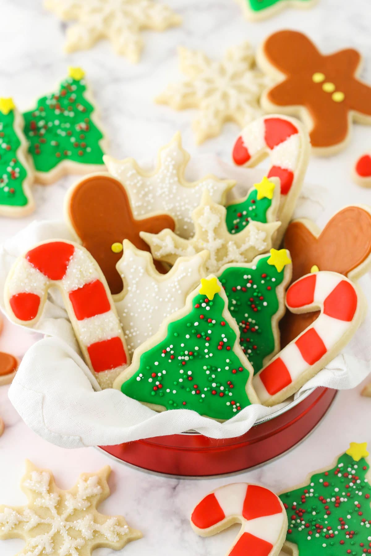 A tin full of holiday-themed sugar cookies decorated with icing on top of a granite countertop