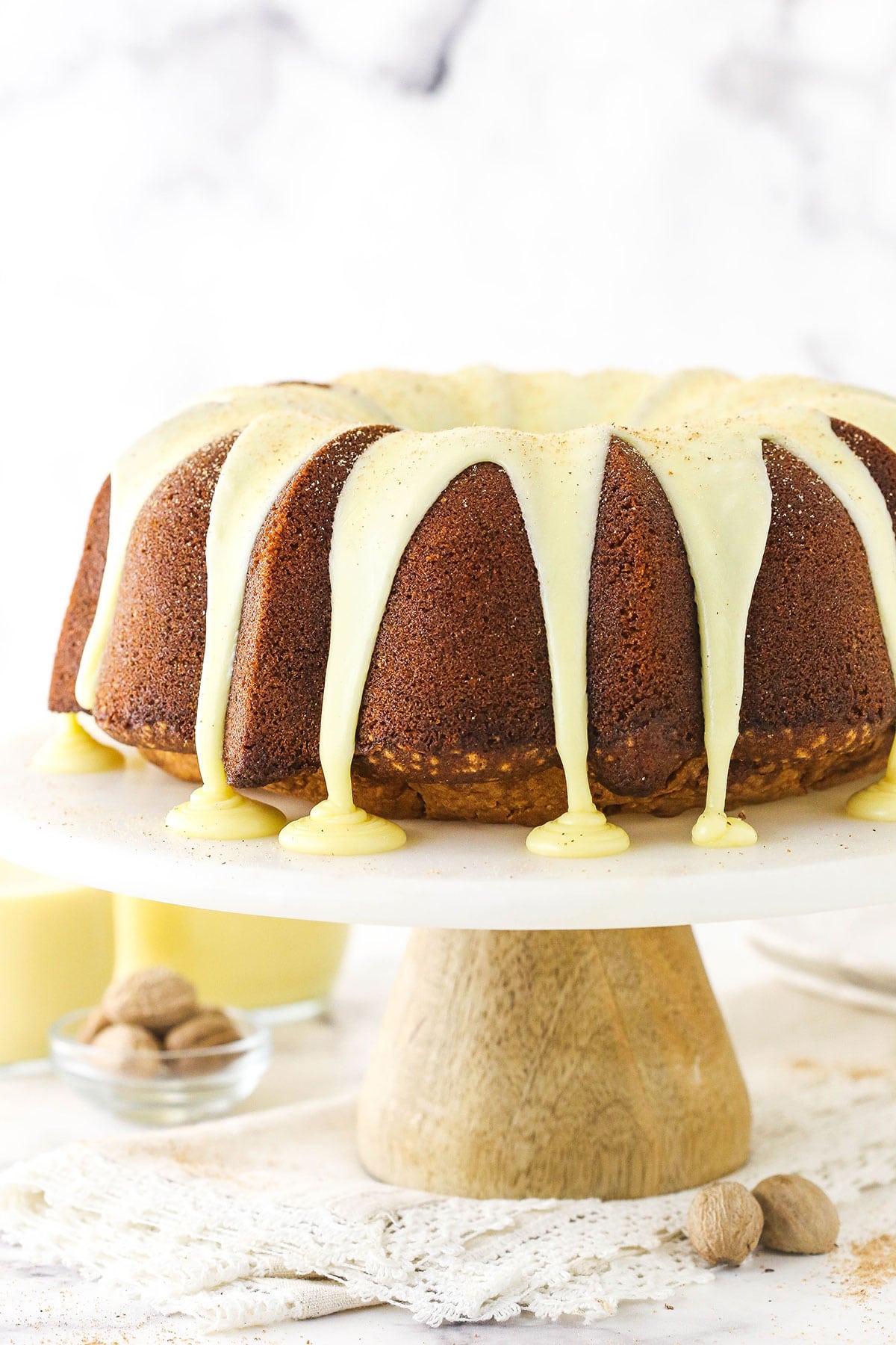 A bundt cake that has just been topped with glaze on a cake stand over a granite countertop