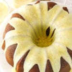 An iced eggnog pound cake on a cake stand with two glasses of eggnog in the background