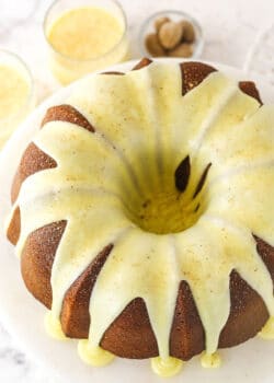 An iced eggnog pound cake on a cake stand with two glasses of eggnog in the background