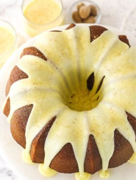 An iced eggnog pound cake on a cake stand with two glasses of eggnog in the background