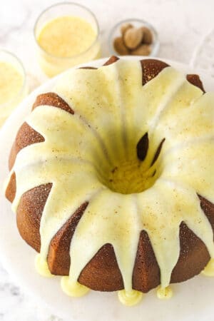 An iced eggnog pound cake on a cake stand with two glasses of eggnog in the background