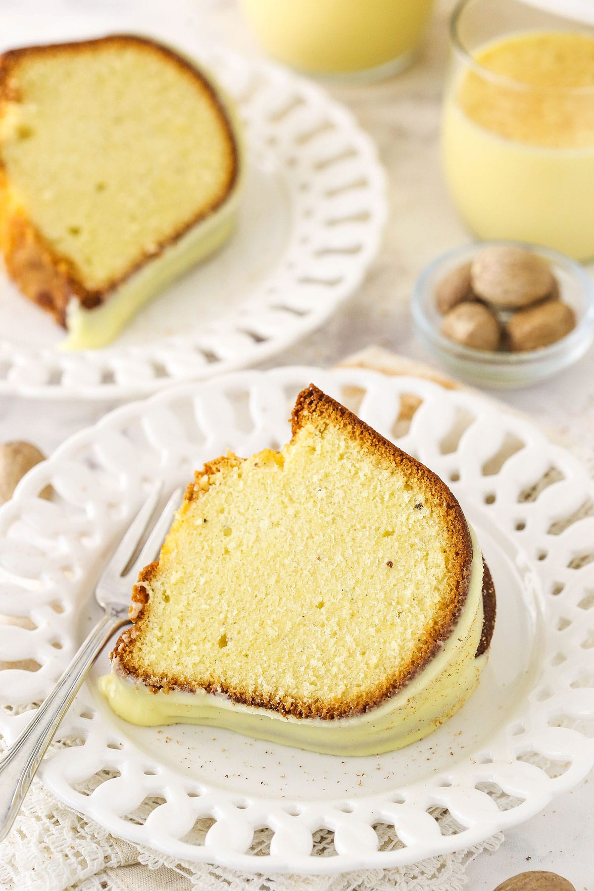 A piece of iced eggnog bundt cake on a plate with a second piece in the background