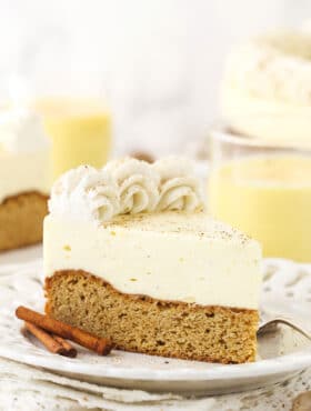 A piece of eggnog blondie cheesecake on a plate with another slice and the remaining cake in the background