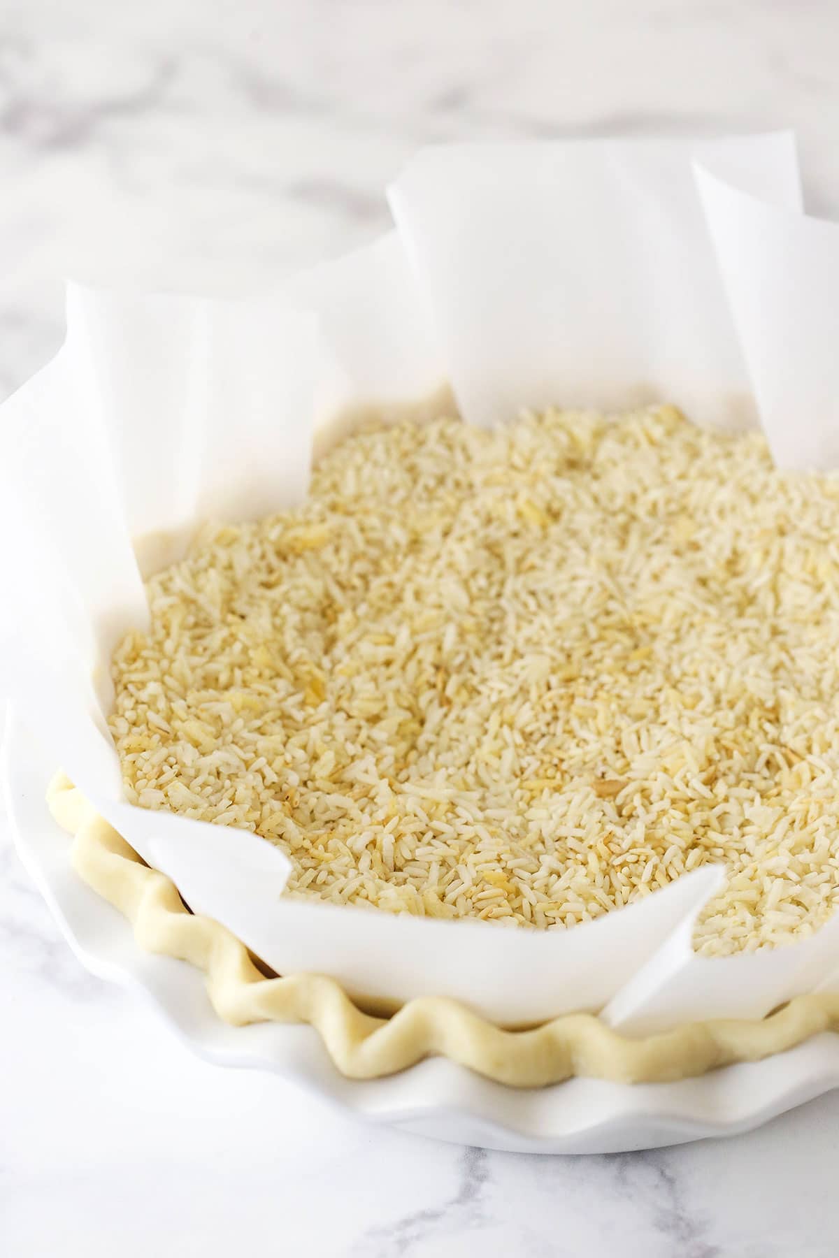 pie crust in white pie plate with parchment paper and rice in it