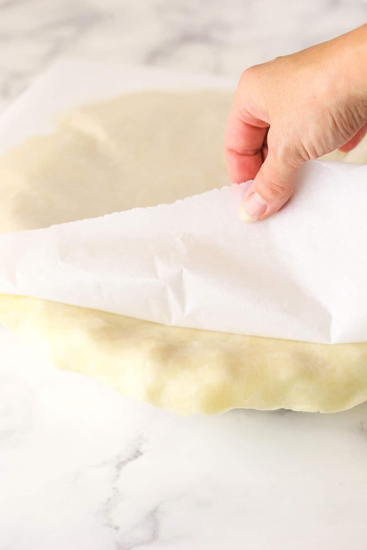 pie crust being added to pie plate with parchment paper being pulled back