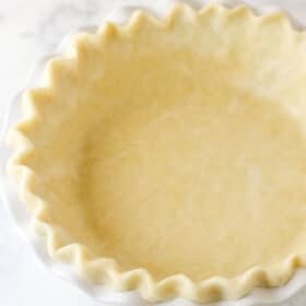 An unbaked all-butter pie crust inside a white pie plate.