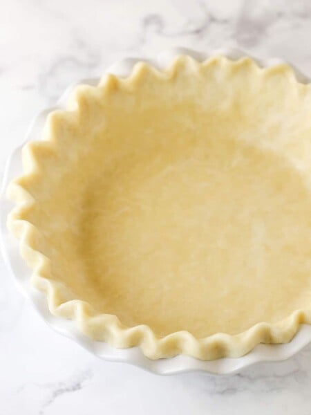 An unbaked all-butter pie crust inside a white pie plate.