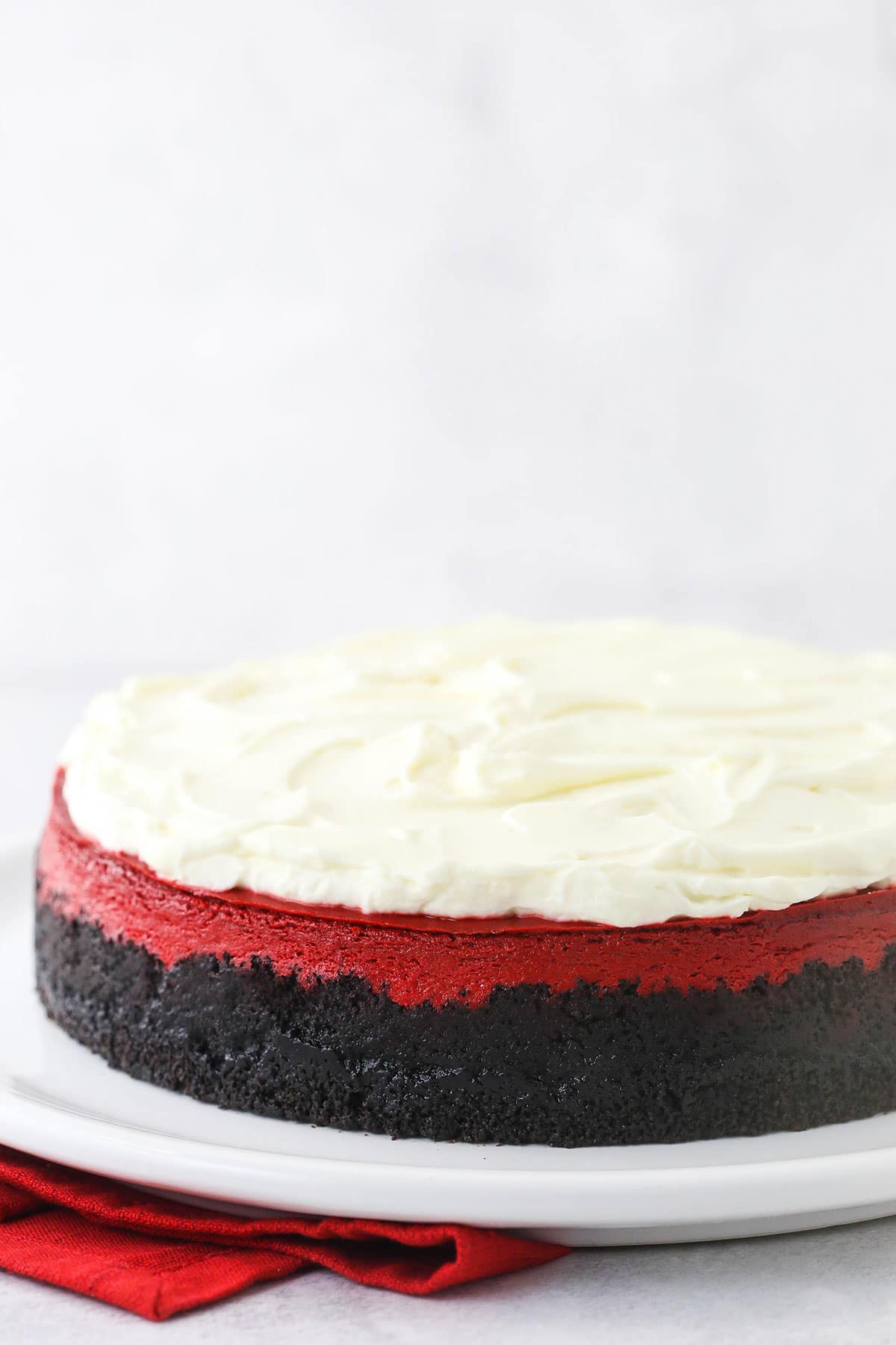 A red velvet cheesecake on a large round serving platter with a red napkin underneath it