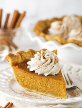 Slice of sweet potato pie on a white plate with whipped cream on top.