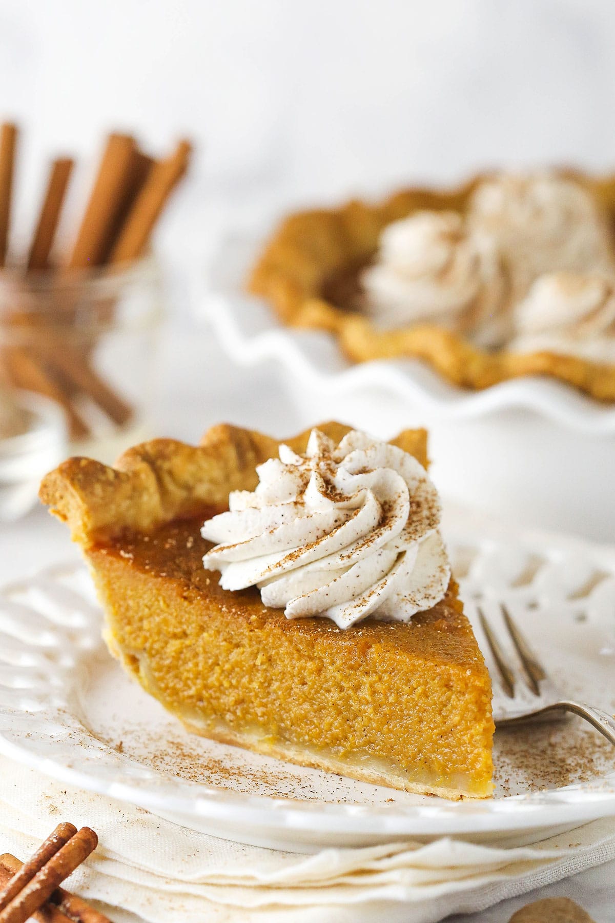 This classic sweet potato pie recipe is made with a flaky crust, browned butter, brown sugar, and the perfect blend of ground spices! Slice of sweet potato pie on a white plate with whipped cream on top.