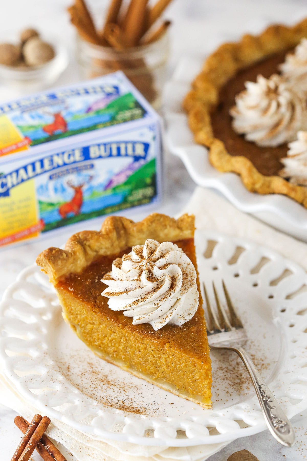 slice of sweet potato pie on white plate with challenge butter in background