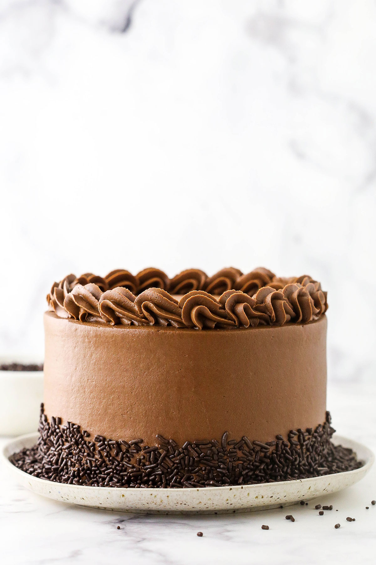 A frosted and decorated 6 inch chocolate cake on a serving platter sitting on a marble countertop