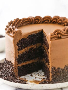 A chocolate layer cake on a speckled cake stand with one slice missing