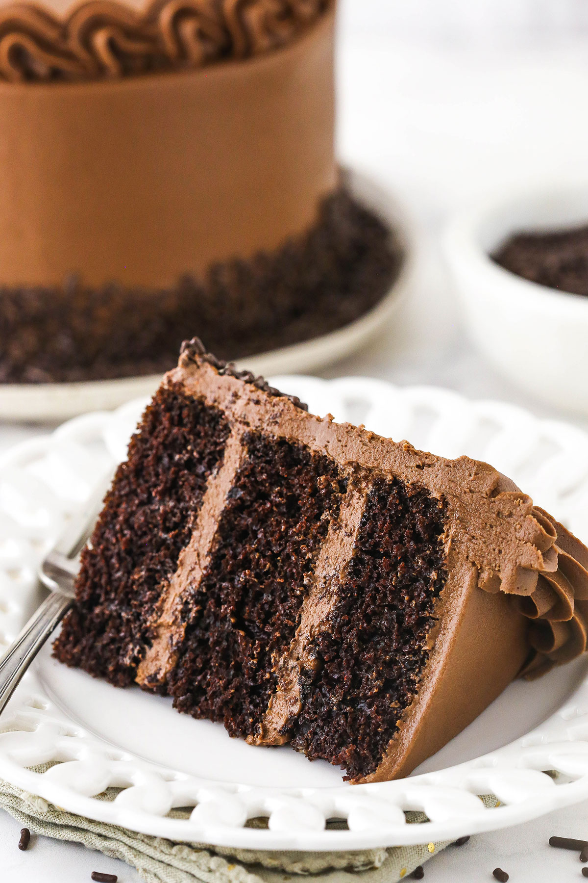 A piece of 6 inch chocolate cake on a plate with the rest of the cake behind it