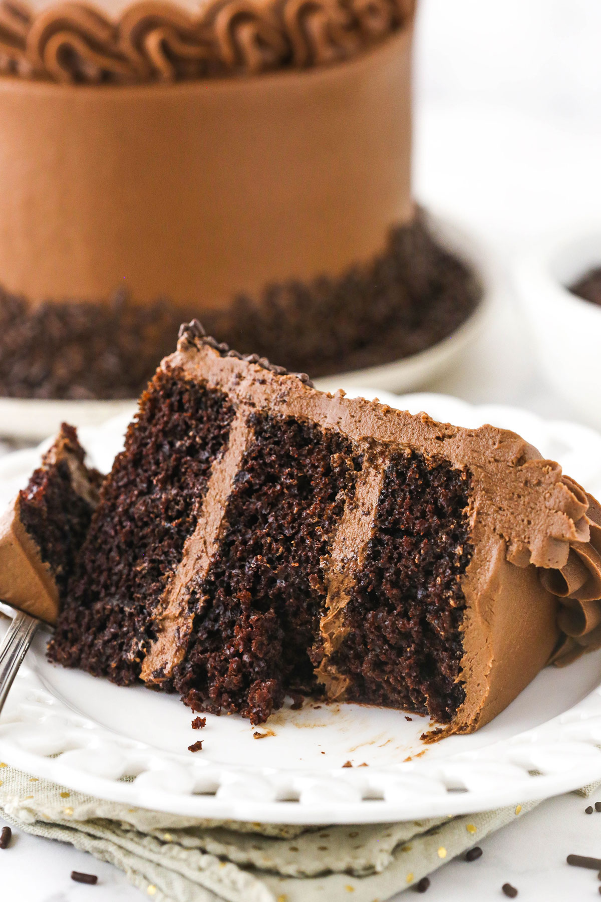 A slice of chocolate layer cake on a plate with a bite on a fork