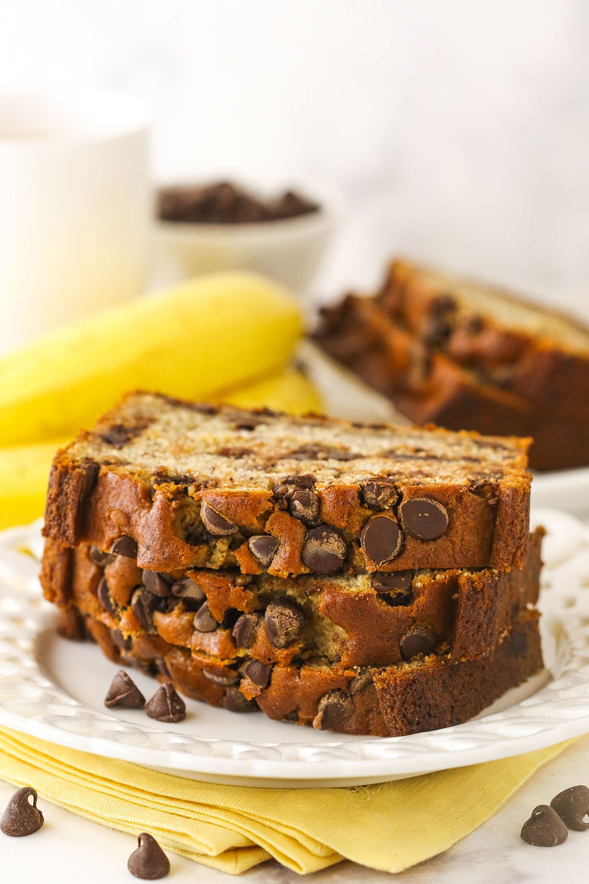 Three slices of banana bread with chocolate chips stacked on top of each other with more bread behind them
