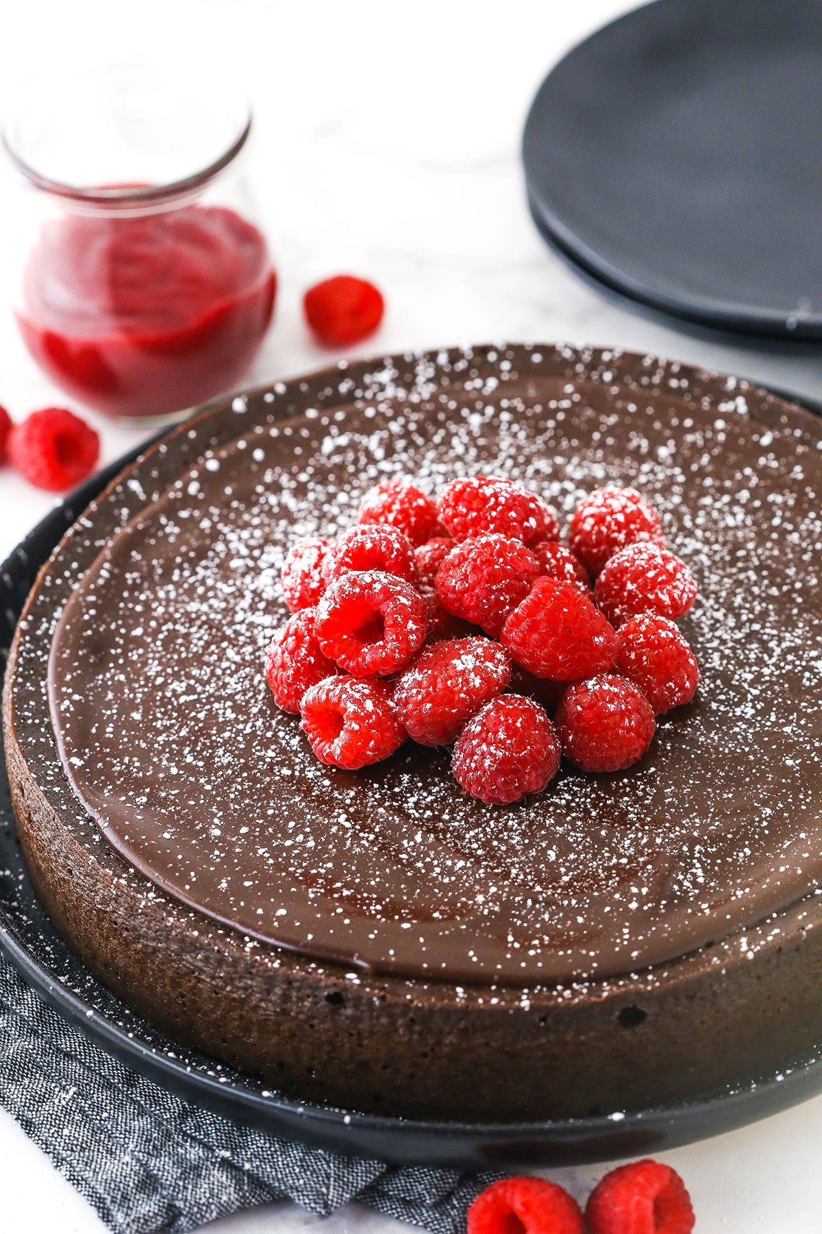 A flourless chocolate torte topped with a dusting of powdered sugar, raspberry sauce and fresh berries