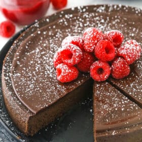 A flourless chocolate torte on a serving platter with two slices cut out of it