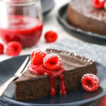 A serving of gluten-free chocolate cake on a plate with raspberry sauce and fresh raspberries on top of it