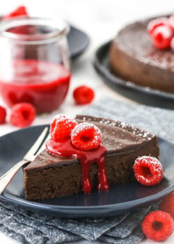 A serving of gluten-free chocolate cake on a plate with raspberry sauce and fresh raspberries on top of it